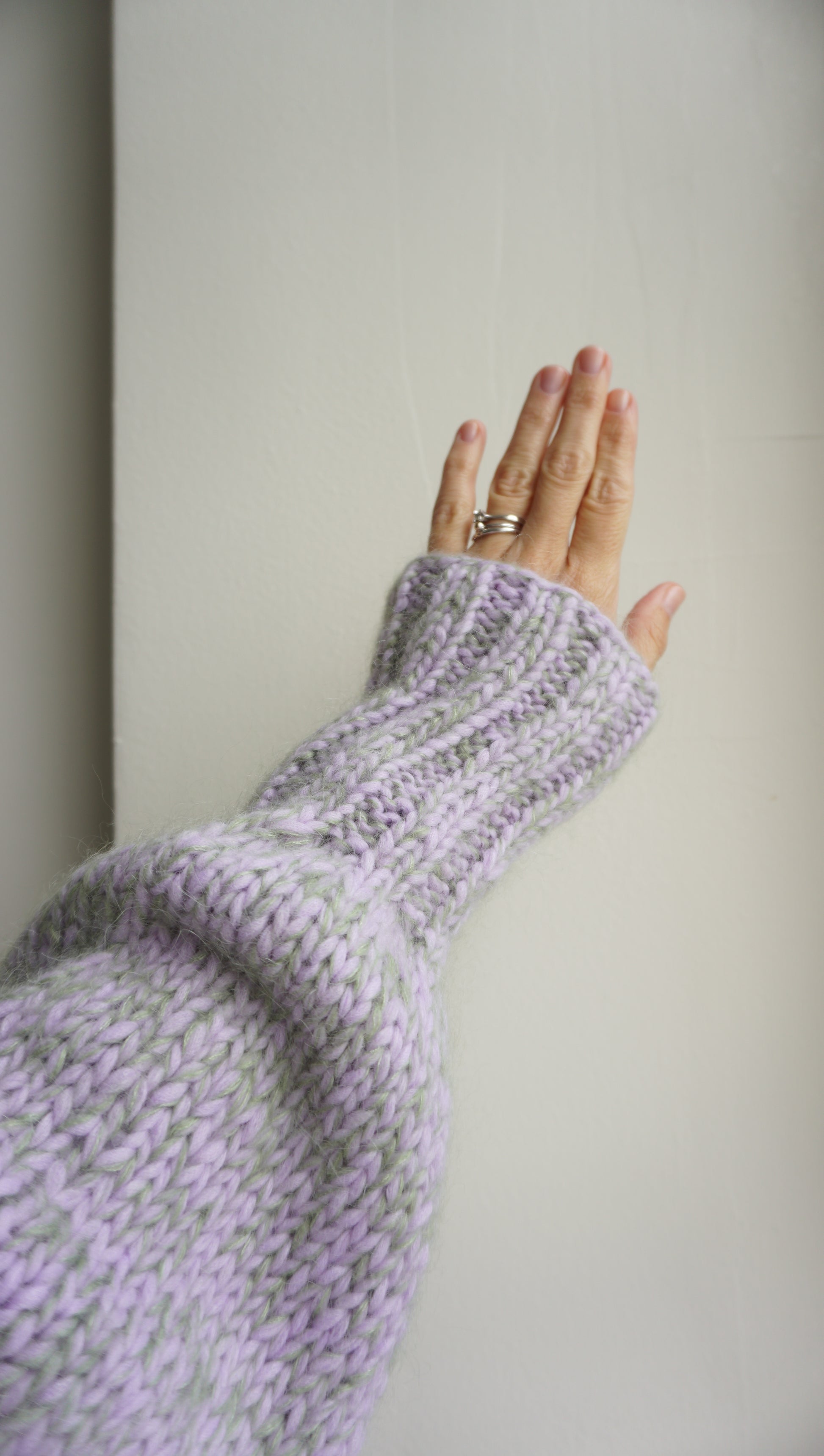 Hand wearing a textured purple sweater cuff against a plain background