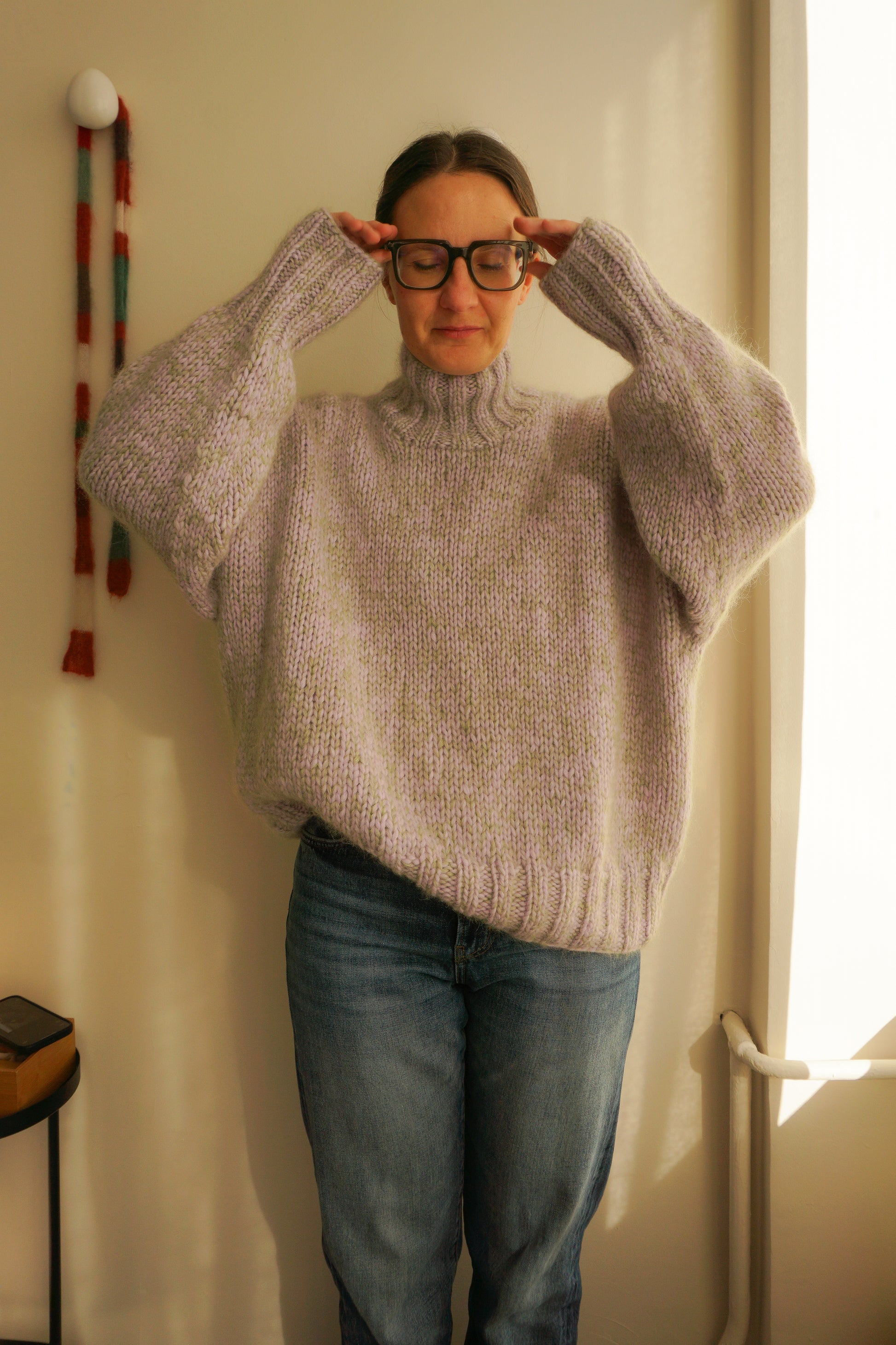 Person wearing a light gray sweater and blue jeans indoors.