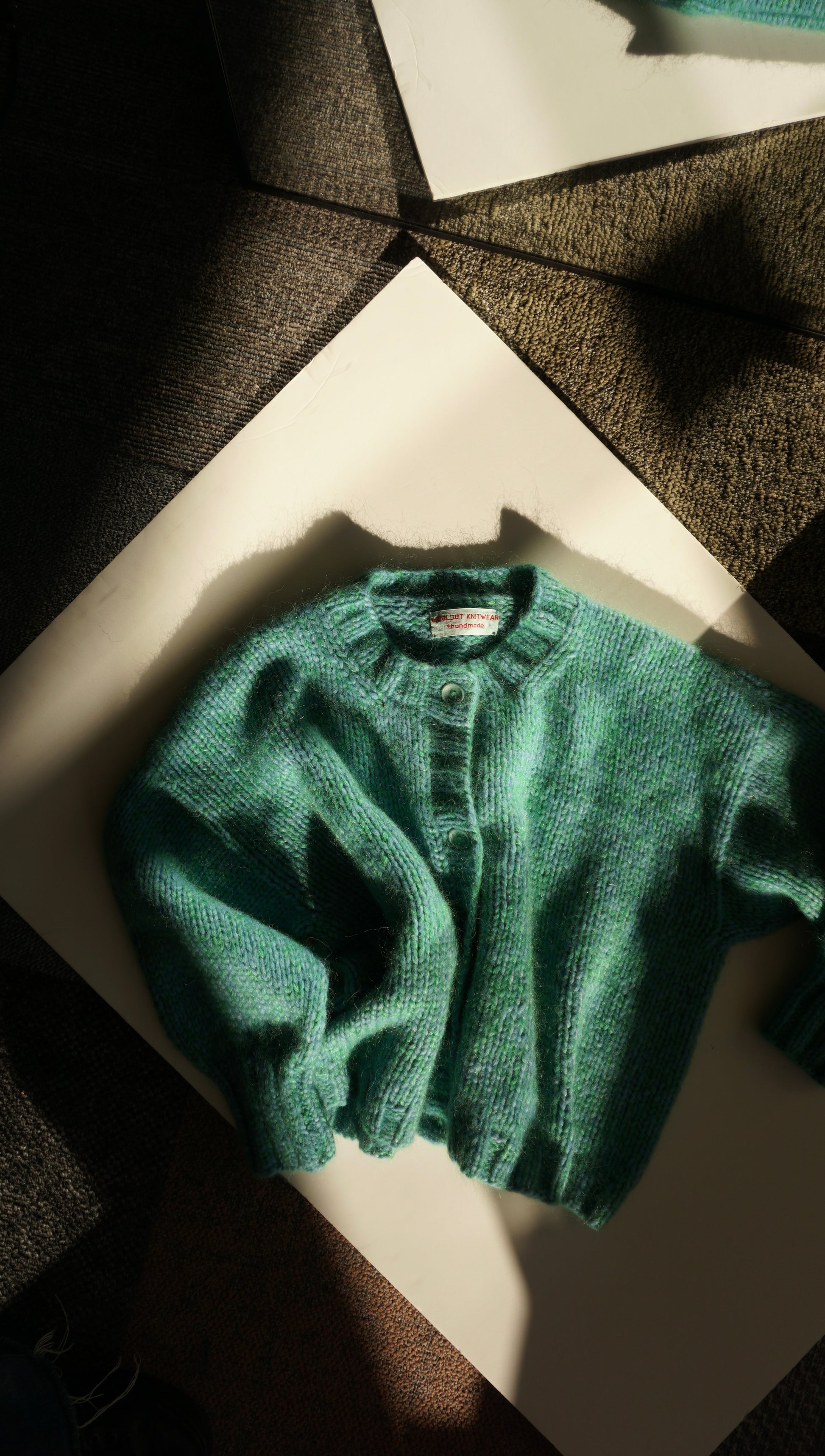 Green sweater on a white surface with a dark geometric patterned background