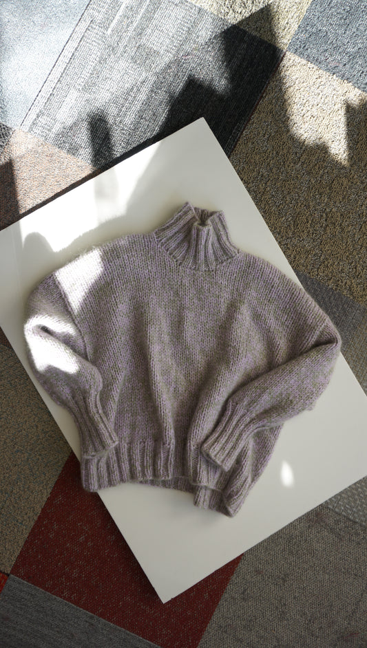 Light violet with green fluff sweater on a white surface with a checkered floor background