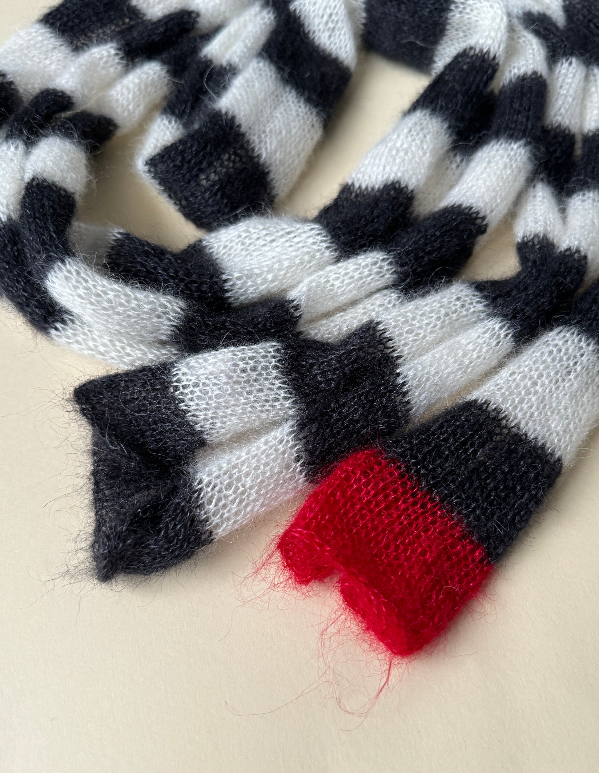 Very long striped black and white skinny thin knitted scarf with red small detail at one end.