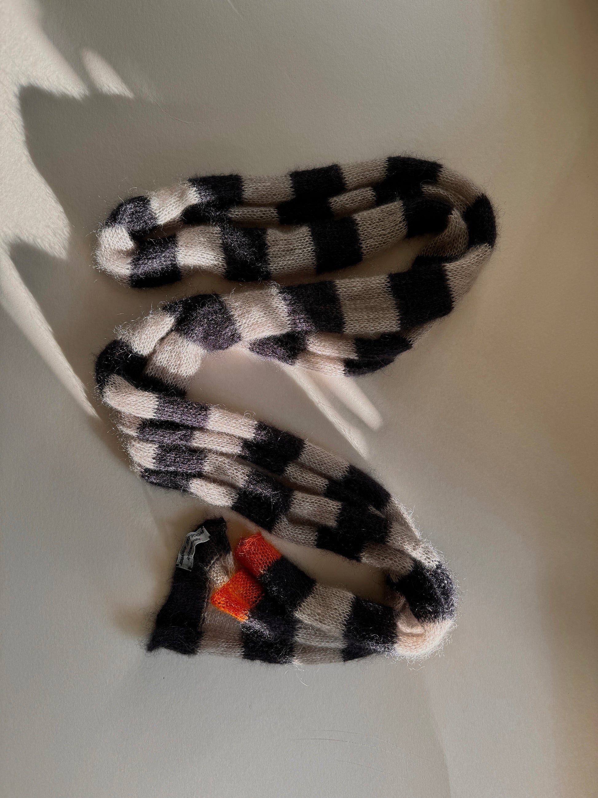 thin skinny long mohair and silk knitted scarf with small orange detail at one end.  in this picture scarf is beautifully enlightened by rays of sun.