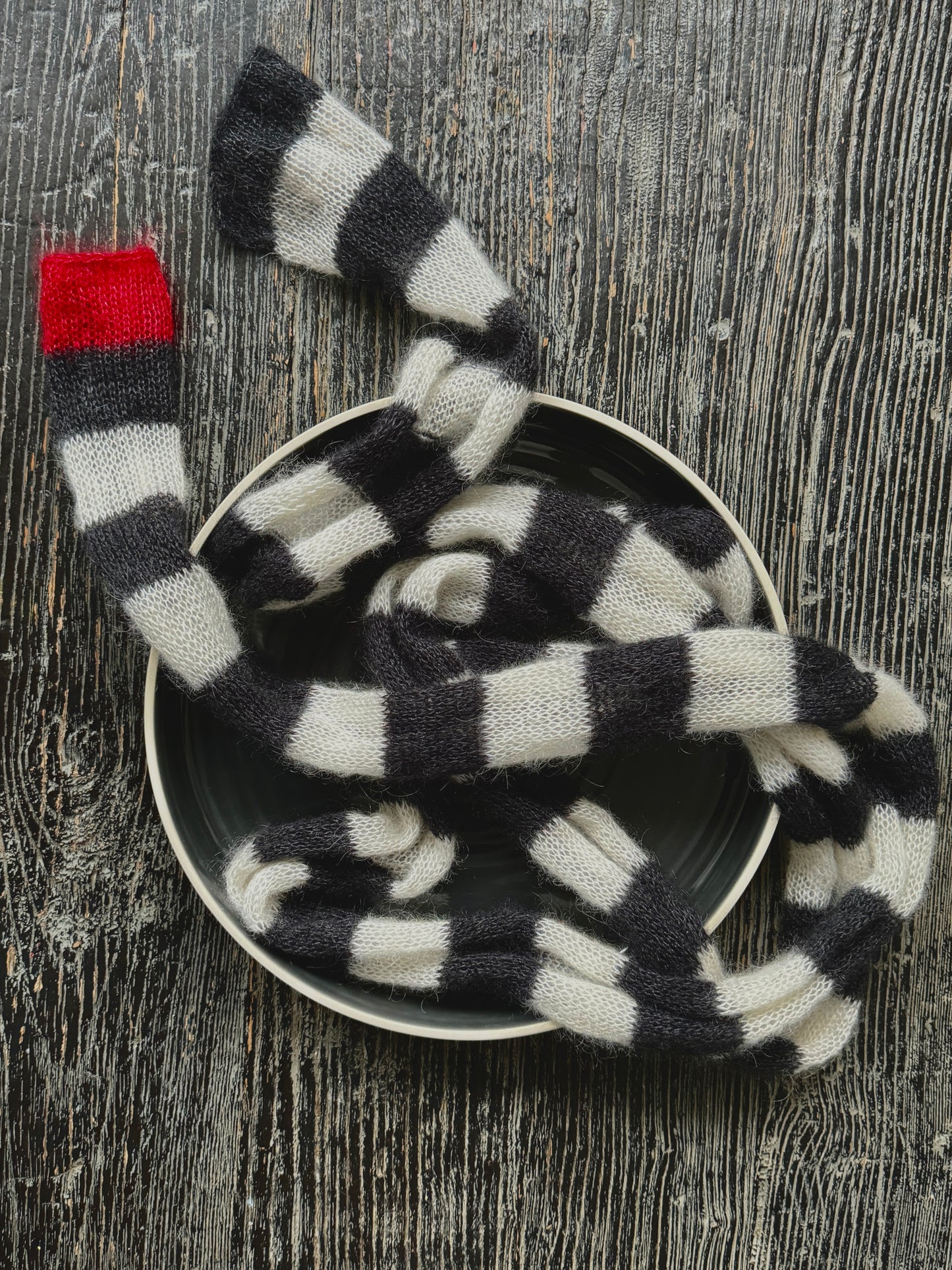 Very long striped black and white skinny thin knitted scarf with red small detail at one end.