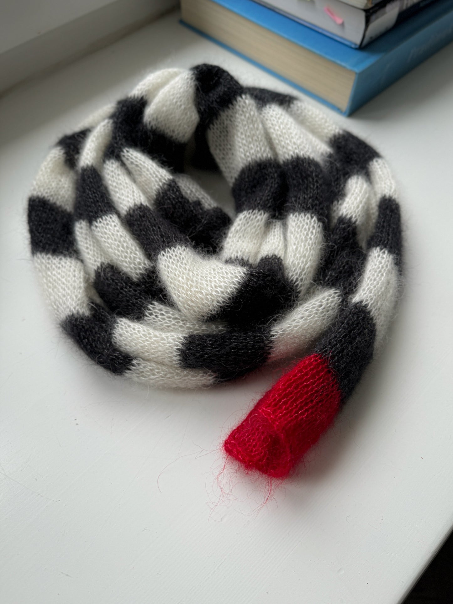 Very long striped black and white skinny thin knitted scarf with red small detail at one end.